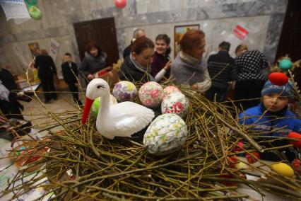 Ребенок смотрит на экспозицию из пасхальных яий и журавля в гнезде.