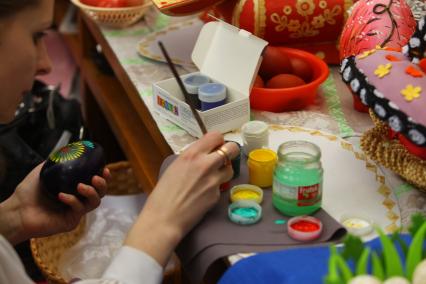 Женщина занимается художественной росписью пасхального яйца красками.