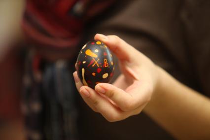 Женская рука держит украшенное пасхальное яйцо.