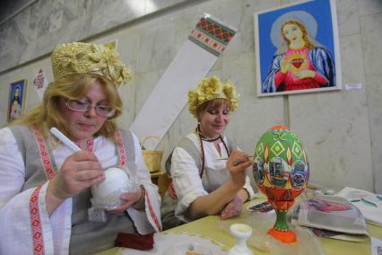 Женщины занимаются художественной росписью пасхальных яйц красками.