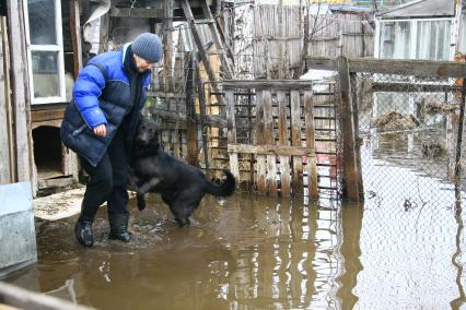 Женщина в резиновых сапогах стоит в воде. Рядом прыгает собака.