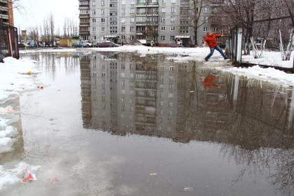 Весенний паводок в городе. Мужчина в ярко красной куртке пытается обойти разлив, карабкается по забору.