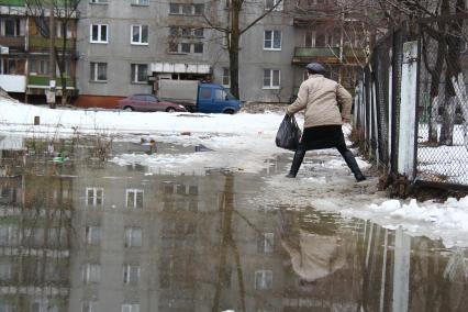 Весенний паводок в городе. Женщина пытается обойти разлив, карабкается по забору.