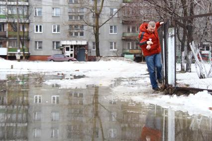 Весенний паводок в городе. Мужчина в ярко красной куртке пытается обойти разлив, карабкается по забору.