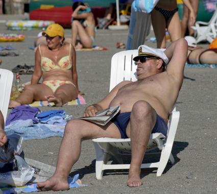 Мужчина сидит на пляже в кресле, наблюдает за отдыхающими.