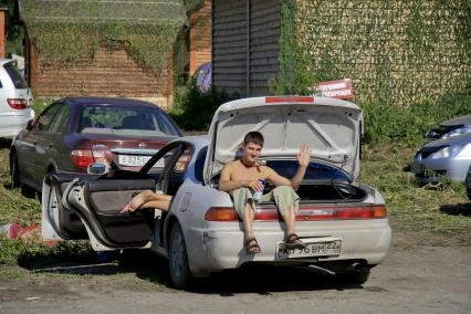 Туристы на автомобиле приехали отдыхать. Мужчина сидит в багажнике автомобиля с банкой пива.