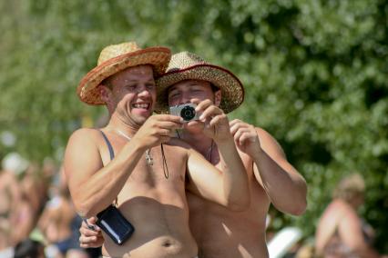 Двое отдыхающих мужчин в соломенных шляпах смеются рассматривая фотографии в фотоаппарате.