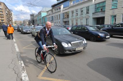 Мужчина едет на велосипеде по обочине автомобильной дороги.