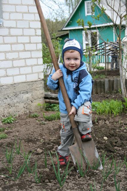 Начало дачного сезона. Ребенок с лопатой вскапывает грядки.