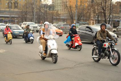 Молодежь едет на скутерах и мопедах по городу.