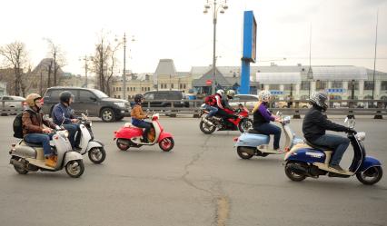 Молодежь едет на скутерах и мопедах по городу.