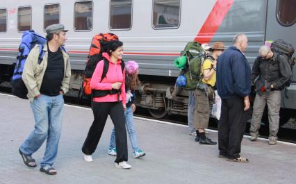По платформе железнодорожного вокзала в Барнауле идет семья с ребенком и туристическими рюкзаками.