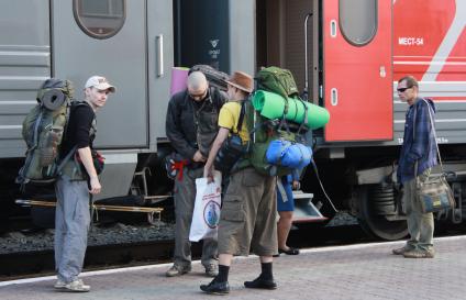 По платформе железнодорожного вокзала в Барнауле люди с туристическими рюкзаками стоят около поезда.