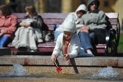 Девочка мокает леденец-петушок в городской фонтан.