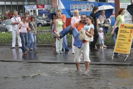 Мужчина переносит девушку через дорогу залитую водой после проливного дождя.