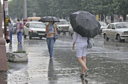 Ливневый дождь на улице города. Девушки идут под зонтами.