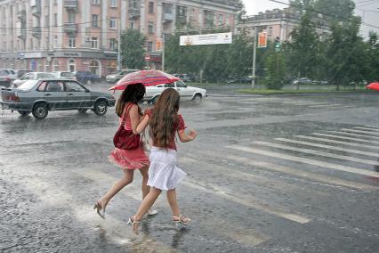 Ливневый дождь на улице города. Две девушки перебегают пешеходный переход под одним зонтом.