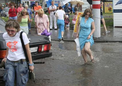 Пешеходы переходят дорогу залитую водой после проливного дождя.