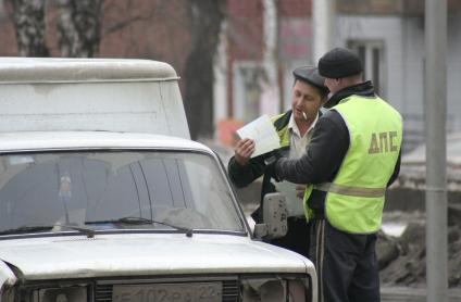 Инспектор ДПС на дороге проверяет у водителя документы.