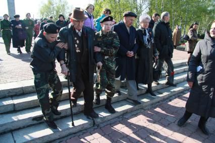 Молодые ребята, дети помогают старику, ветерану спускаться по лестнице.