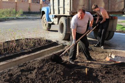 Сотрудники коммунального хозяйства занимаются озеленением улиц города. На снимке люди насыпают плодородный слой почвы.