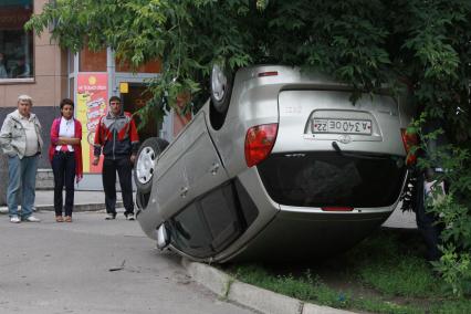 ДТП в котором перевернулся автомобиль. Люди смотрят на перевернутую машину.