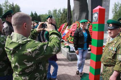 Девушка фотографируется в берете пограничника рядом с пограничным столбом.