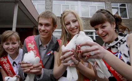 Выпускники школы держат в руках белых голубей.