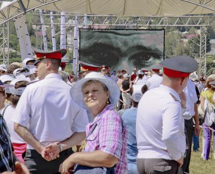 В селе Сростки, алтайского края на горе Пикет проходят шукшинские чтения. На большом экране крупно показаны глаза Василия Шукшина. На переднем плане двое полицейских и женщина.