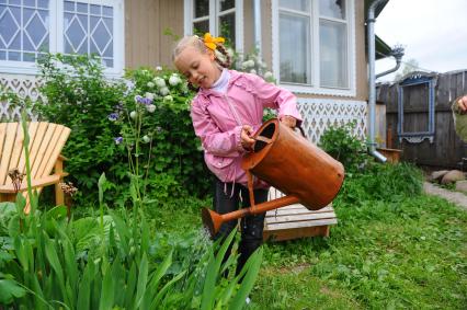 Девочка на даче занимается поливом из лейки.