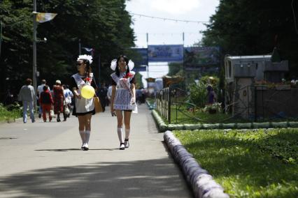 Две девушки в школьной форме идут по улице города. Одна из них держит в руках воздушный шарик.
