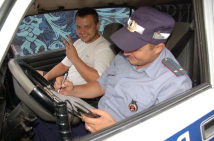 Мужчина водитель сидит в машине инспектора ДПС, инспектор составляет протокол.