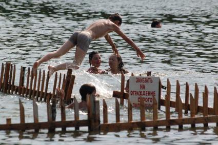 Мальчик прыгает в воду с ограждения на котором прикреплена надпись: `Залезать на ограждение строго запрещено`.