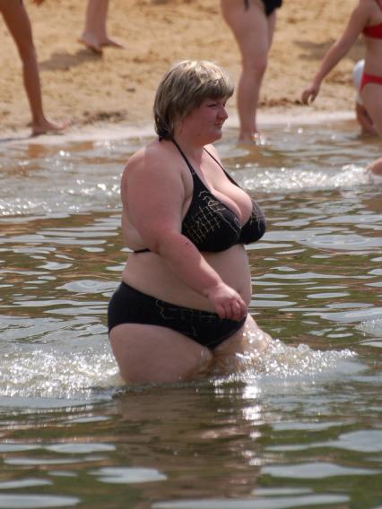 Девушка с избыточным весом заходит купаться в воду.