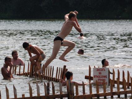 Мальчик прыгает в воду с ограждения на котором прикреплена надпись: `Залезать на ограждение строго запрещено`.