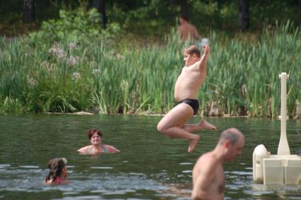 Тучный мальчик прыгает с берега в воду.