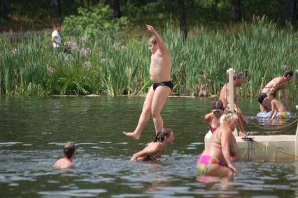 Тучный мальчик прыгает с берега в воду.