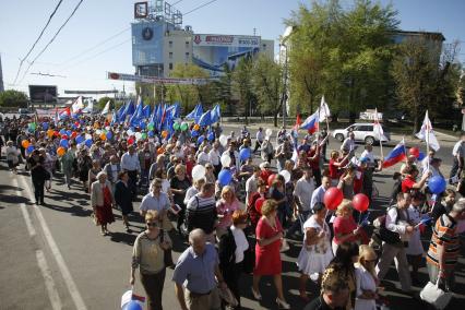 Первомайская демонстрация на улицах города. Люди идут с надувными шариками и флагами.