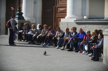 Иностранные туристы сидят на бордюре перед входом в Кремль.