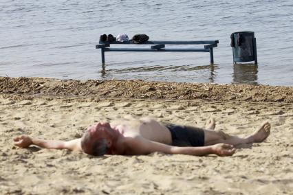 Мужчина загорающий на пляже. В воде стоит скамейка на которой лежат его личные вещи.