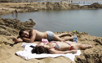Молодая пара (мужчина и женщина) загорают на пляже.