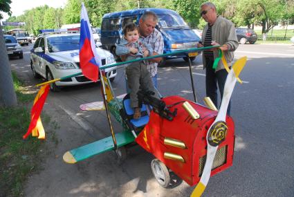 Мужчина усаживает ребенка в коляску похожую на самолет с пропеллером.