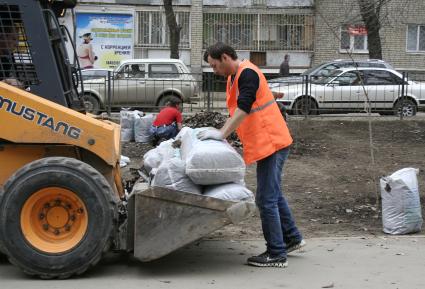 Мужчина складывает мешки с собранной прошлогодней листвой на погрузчик.