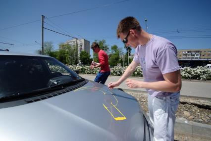 Мужчина рисует на капоте автомобиля серп.