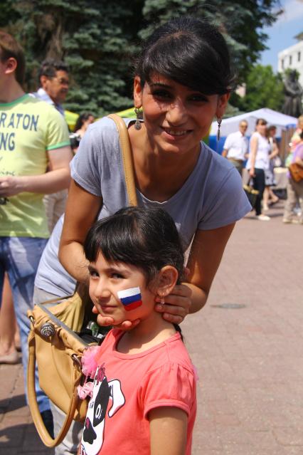 Люди отмечают праздник День России в Нижнем Новгороде. На снимке: женщина с ребенком южной внешности с нарисованным на шеке флагом России.