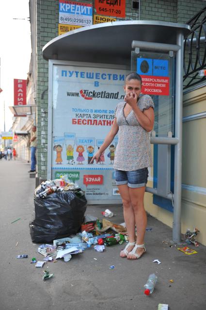 Мусор на улице города. На снимке: девушка на автобусной остановке.