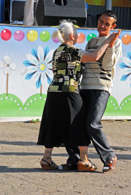 Танцующие люди на улице, в честь открытия парка. На снимке пара пожилых людей ( мужчина и женщина ) танцуют вальс.