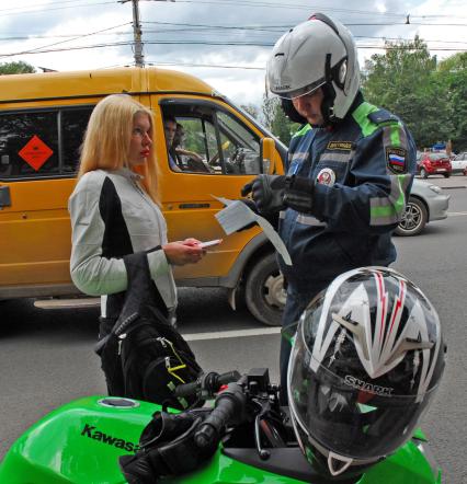 Сотрудник полиции на мотоцикле проверяет у девушки документы.