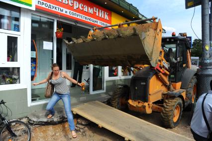 Люди выходям из магазина,двери которого загородил ковш бульдозера.