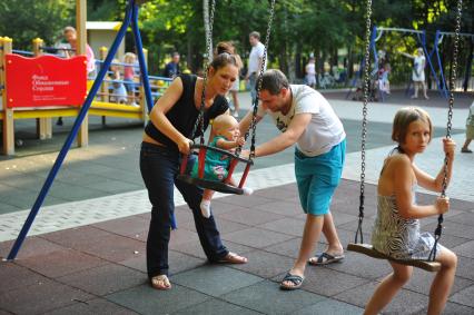 Парк `Сокольники`. На снимке: родители катают ребенка на качелях.